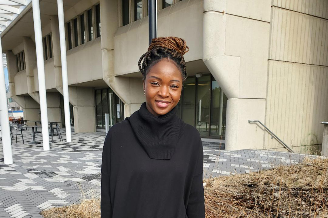 Thelma Abu in a black turtle neck, with copper-coloured box-braids in a large bun, standing on UTM campus