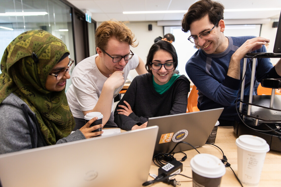 4 engineering students looking a laptop, smiling