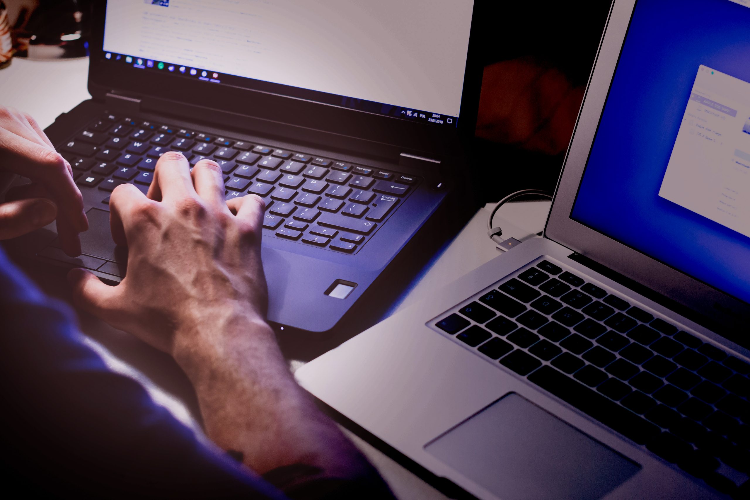 White masc hands on a laptop keyboard, with a second laptop off to the side